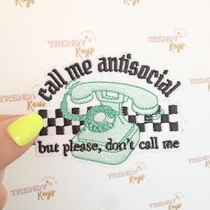 May include: Embroidered patch with a mint green telephone design and the phrase "call me antisocial but please, don't call me" in black text. The patch has a black and white checkered border.