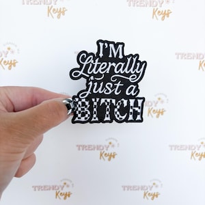 May include: A black and white patch with the text "I'M Literally just a BITCH". The word "BITCH" is in a black and white checkered pattern. The patch is held by a hand against a white background.