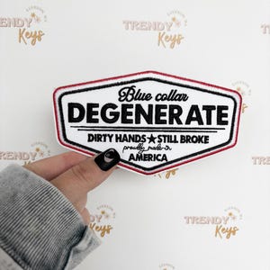 May include: Embroidered patch with the text "Blue collar DEGENERATE" in black on a white background, framed by a red and black border. The patch also includes the text "DIRTY HANDS STILL BROKE proudly made in AMERICA".