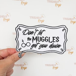 May include: A white patch with a black border and the text "Don't let the Muggles get you down." The patch features a lightning bolt and glasses graphic. The background has a repeating pattern of the words "TRENDY Keys".