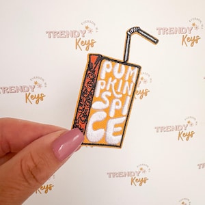 May include: Embroidered patch in the shape of a juice box with the words "PUMPKIN SPICE" in white. The juice box is orange and white with a black and orange patterned side and a black and white striped straw.