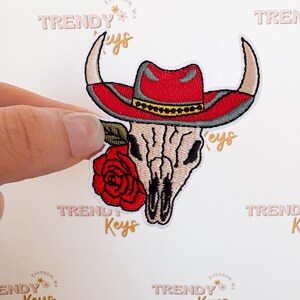 May include: Embroidered patch featuring a white skull wearing a red cowboy hat with a yellow band, a red rose, and the text "TRENDY Keys" in pink and gold.