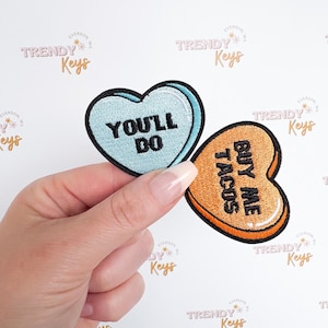 May include: Two heart-shaped embroidered patches. One is light blue with the text "You'll Do" and the other is orange with the text "Buy Me Tacos".