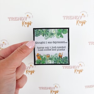 May include: A small, square patch with a black border, featuring text and illustrations. The text reads "thought i was depressed... turns out i just needed iced coffee and plants." The design includes green tropical leaves and iced coffee illustrations.