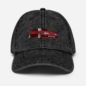 Puede incluir: Una gorra de béisbol de denim negro con una imagen bordada en rojo de un coche deportivo.