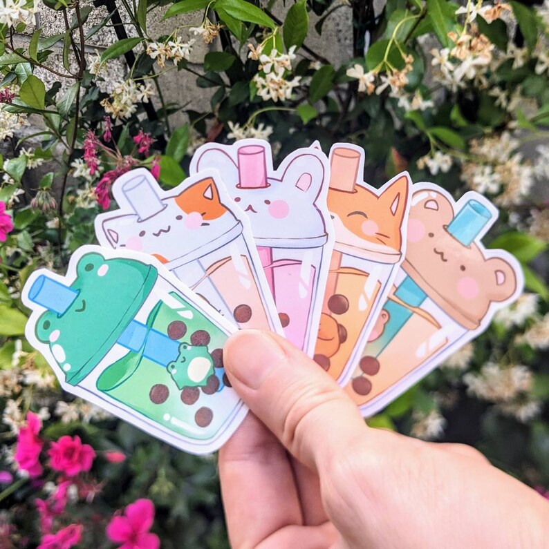May include: Five colorful bubble tea stickers with different animal faces. The stickers feature a frog, a cat, a bunny, a bear, and a cat. Each sticker has a straw and boba pearls inside the cup.
