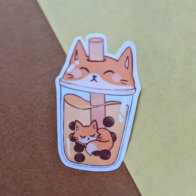 May include: A sticker of a cartoon fox sleeping inside a boba tea cup with tapioca pearls. The fox is orange and white with a brown nose and closed eyes. The boba tea is brown with a clear plastic cup and a straw.