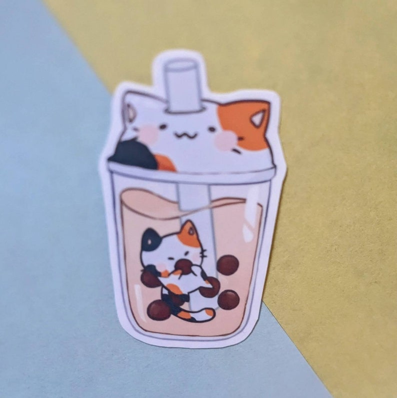 May include: A sticker of a cat inside a boba tea cup. The cat is orange, white, and black with a black nose and a pink tongue. The boba tea is brown with white milk and black boba pearls.