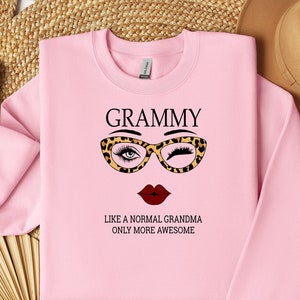 May include: Pink sweatshirt with the text "GRAMMY LIKE A NORMAL GRANDMA ONLY MORE AWESOME" and a graphic of a woman wearing glasses and a red lipstick.