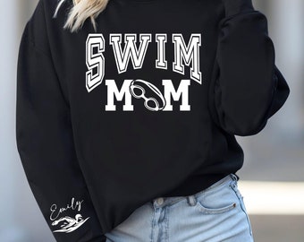 May include: Black sweatshirt with white text that reads "SWIM MOM" with a pair of swimming goggles in the middle of the word "MOM". The left sleeve has a white graphic of a swimmer and the text "Emily".