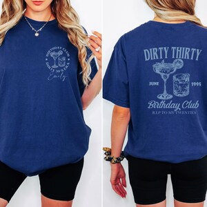 May include: Navy blue t-shirt with front and back graphics. The front has a cocktail design and the text "Birthday Club Dirty 30's Era Emily". The back shows "Dirty Thirty", cocktail graphics, the date "June 1995", and "Birthday Club R.I.P. to my twenties".