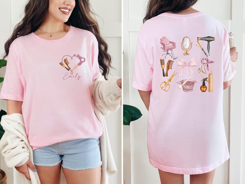 Op de afbeelding: Lichtroze t-shirt met een hartvormig ontwerp met haarstylingtools en de naam "Emily". De achterkant van het shirt toont diverse salon tools en accessoires, waaronder een stoel, spiegel en schaar.