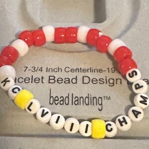 Puede incluir: Un brazalete de cuentas blancas y rojas con la palabra "CLEVELAND CHAMPS" escrita en letras negras sobre cuentas blancas. El brazalete tiene una circunferencia de 19,7 cm y est&aacute; hecho por bead landing.