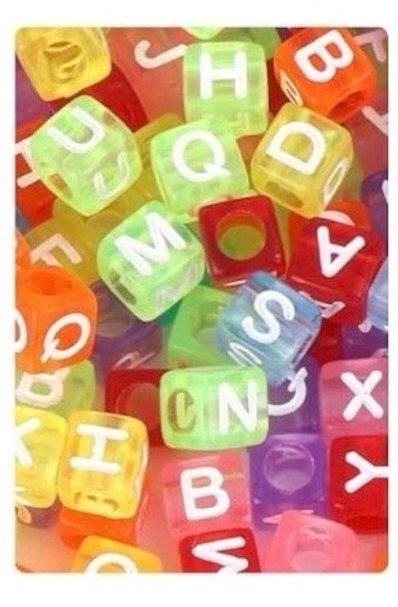 Puede incluir: Primer plano de cuentas de letras del alfabeto de colores. Las cuentas est&aacute;n hechas de pl&aacute;stico transl&uacute;cido y tienen letras blancas. Las cuentas son de varios colores, incluyendo rojo, naranja, amarillo, verde, azul y morado.