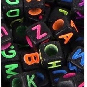 Puede incluir: Primer plano de cuentas de letras negras con letras de colores ne&oacute;n. Las cuentas est&aacute;n en un mont&oacute;n y algunas est&aacute;n apiladas unas sobre otras.