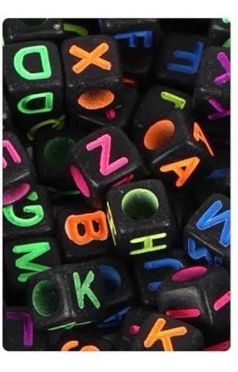 Puede incluir: Primer plano de cuentas de letras negras con letras de colores ne&oacute;n. Las cuentas est&aacute;n en un mont&oacute;n y algunas est&aacute;n apiladas unas sobre otras.