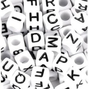 Puede incluir: Primer plano de un mont&oacute;n de cuentas de letras de pl&aacute;stico blanco. Las cuentas son todas del mismo tama&ntilde;o y forma, y est&aacute;n dispuestas en un orden aleatorio. Las letras en las cuentas son negras y todas en may&uacute;sculas.