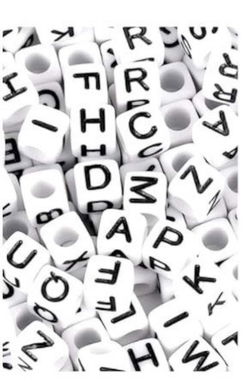 Puede incluir: Primer plano de un mont&oacute;n de cuentas de letras de pl&aacute;stico blanco. Las cuentas son todas del mismo tama&ntilde;o y forma, y est&aacute;n dispuestas en un orden aleatorio. Las letras en las cuentas son negras y todas en may&uacute;sculas.