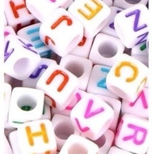 Puede incluir: Un mont&oacute;n de cuentas de letras de pl&aacute;stico blanco con letras de colores. Las cuentas miden aproximadamente 1 cm y tienen un agujero en el centro para enhebrar.