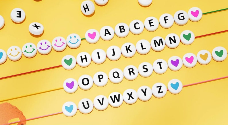 Puede incluir: Cuentas de alfabeto blancas con letras negras y cuentas de coraz&oacute;n y caritas sonrientes de colores enhebradas en una cuerda. Las cuentas est&aacute;n dispuestas en orden alfab&eacute;tico.