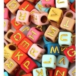 Puede incluir: Primer plano de cuentas de letras del alfabeto de colores. Las cuentas son de pl&aacute;stico y tienen un acabado mate. Las letras son doradas.