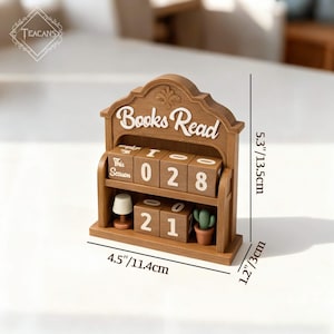Puede incluir: Un calendario de escritorio de madera con las palabras "Books Read" en escritura blanca. El calendario muestra los n&uacute;meros "028" y "21" en bloques giratorios. Incluye una peque&ntilde;a l&aacute;mpara y un cactus en maceta. El calendario mide 11,4 cm de ancho, 13,5 cm de alto y 3 cm de profundidad.