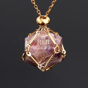 May include: A gold necklace with a purple amethyst gemstone d20 dice pendant. The dice has a gold cage around it and is engraved with "R&B" and the date "05.24.2024".