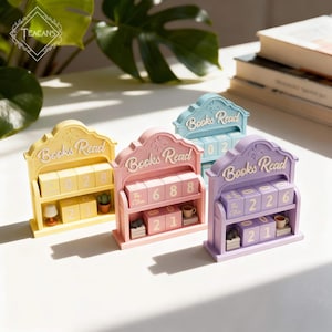 May include: Four pastel-coloured wooden book-shaped calendars with the words "Books Read" on top. Each calendar has a shelf with numbered blocks and miniature decor. The colours are yellow, pink, blue, and purple.