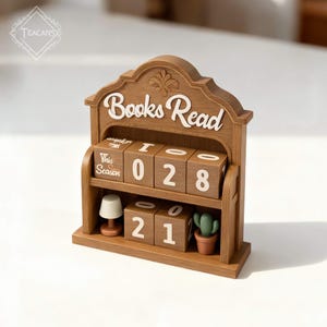 May include: A wooden "Books Read" calendar with rotating number blocks. The blocks display the numbers "028" and "21". A small lamp and a potted cactus are on the shelf. The text "This Season" is also visible.