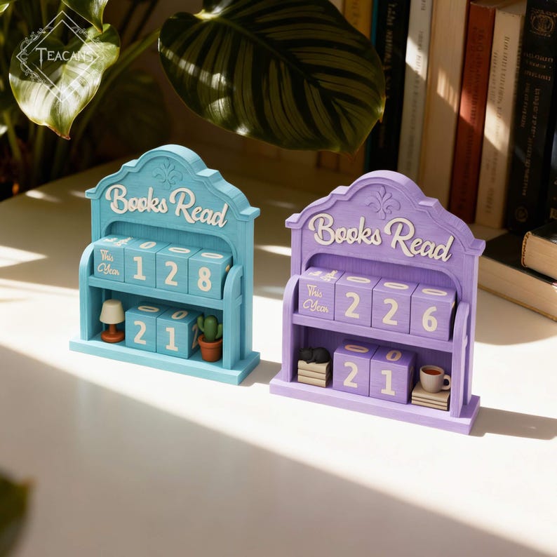 Puede incluir: Dos calendarios de madera "Books Read" en azul claro y lavanda. Cada uno tiene un estante con bloques num&eacute;ricos para rastrear los libros le&iacute;dos, adem&aacute;s de una decoraci&oacute;n en miniatura como una l&aacute;mpara, un cactus y una taza de caf&eacute;. El texto "Books Read" est&aacute; arqueado en la parte superior.