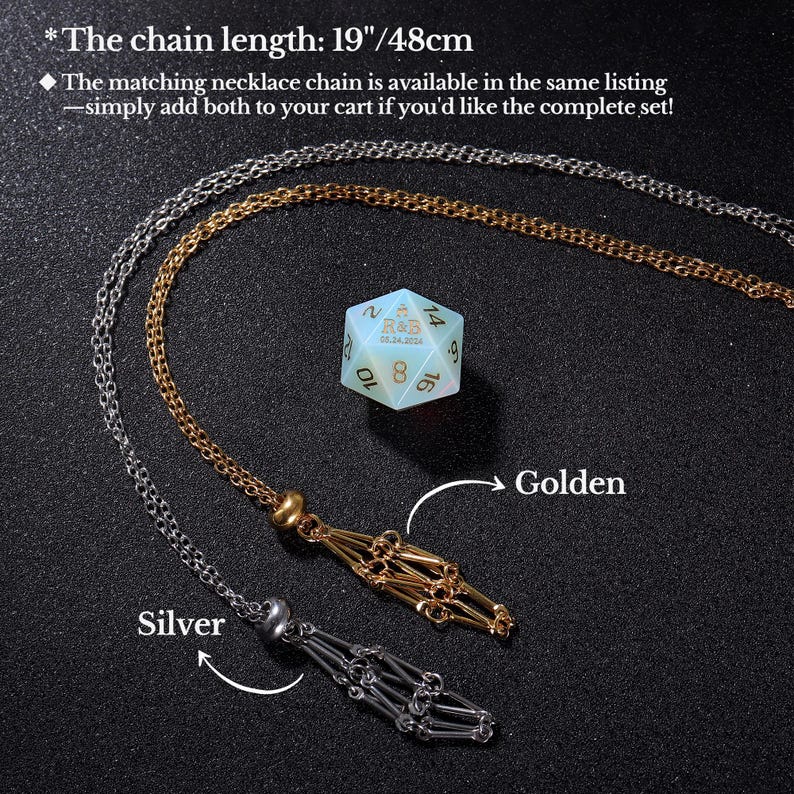 May include: Two necklace chains, one silver and one gold, with a decorative tassel at the end. The chains are displayed against a black background with a light blue and gold 20-sided die in the centre. The chain length is 19 inches or 48 centimetres.