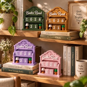 May include: Four decorative shelf-top book trackers in green, orange, purple, and pink. Each features the text Books Read, a This Year label, numbered blocks for tracking, and miniature lamp and cactus figurines. These items sit on wooden shelves.