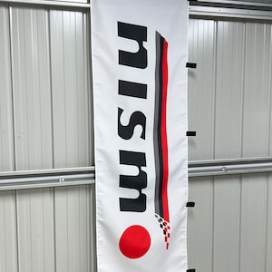 May include: A white banner with the word "NISSAN" in black letters. The banner has a red circle with a checkered pattern in the bottom right corner.