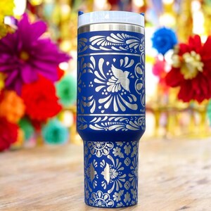 May include: A blue stainless steel tumbler with a silver floral design. The tumbler has a lid and is decorated with a traditional Mexican folk art pattern.
