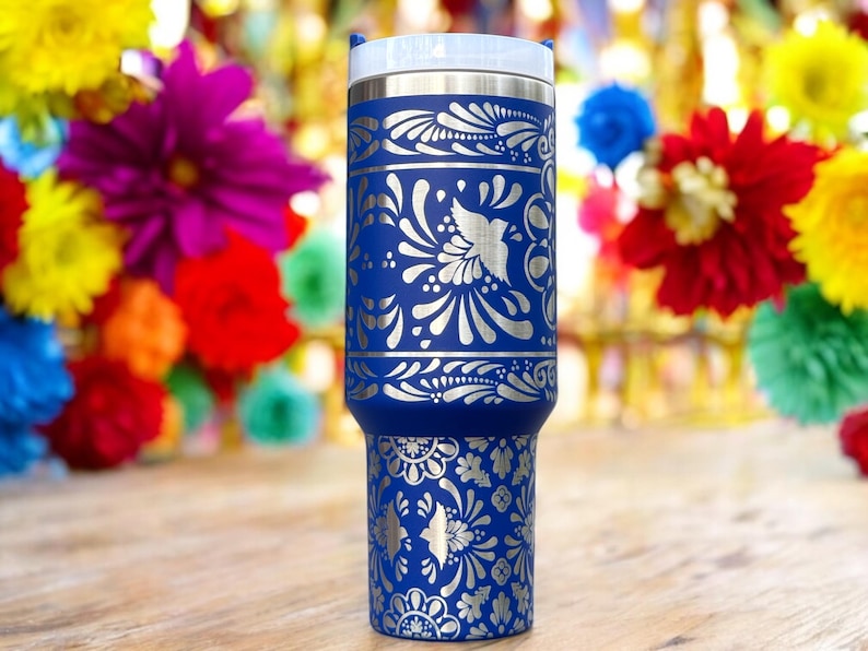 May include: A blue stainless steel tumbler with a silver floral design. The tumbler has a lid and is decorated with a traditional Mexican folk art pattern.