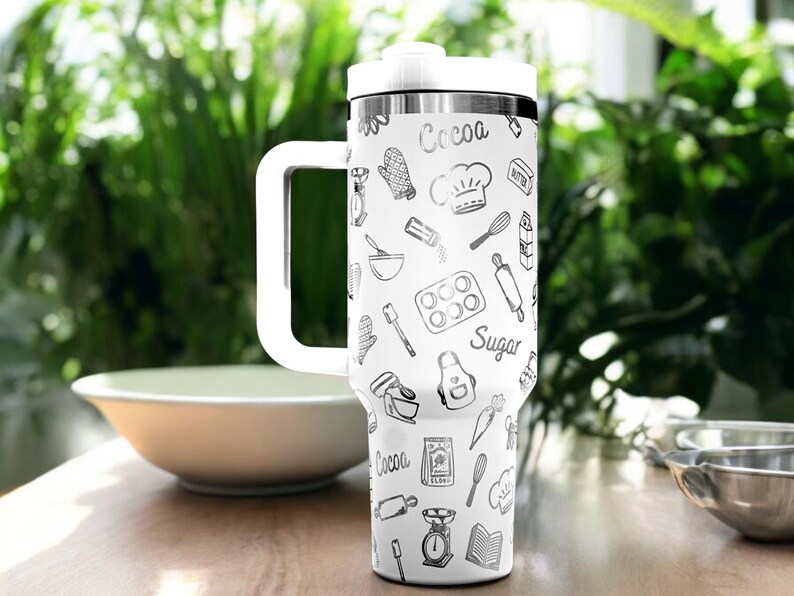May include: White travel mug with a black and white pattern of baking-themed illustrations. The mug has a black lid and a black handle. The text "Cocoa" and "Sugar" are visible on the mug.