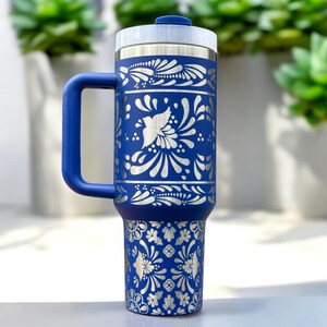 May include: A blue stainless steel travel mug with a white floral design. The mug has a handle and a lid.