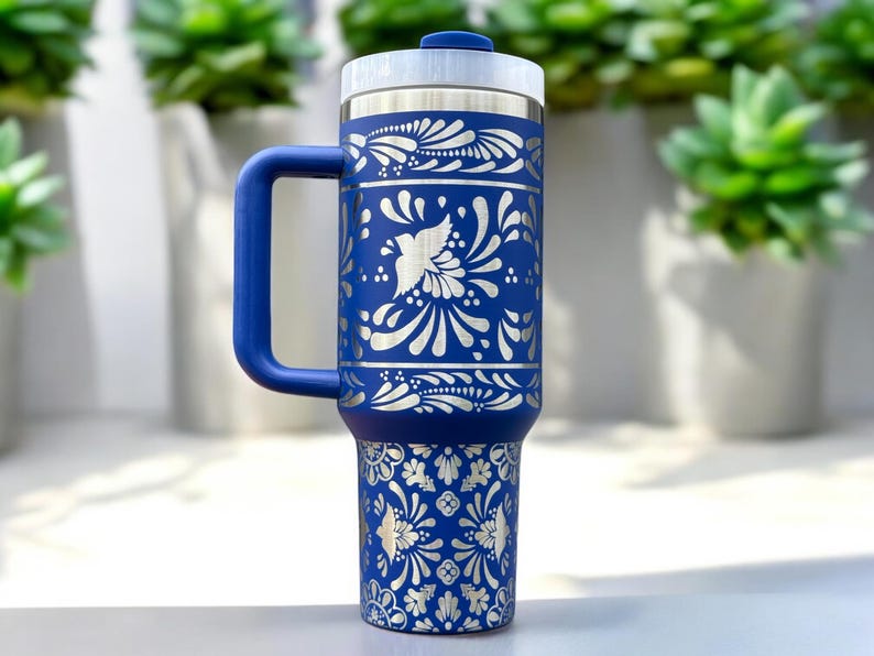 May include: A blue stainless steel travel mug with a white floral design. The mug has a handle and a lid.