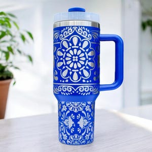 May include: A blue stainless steel travel mug with a white floral design. The mug has a handle and a lid.