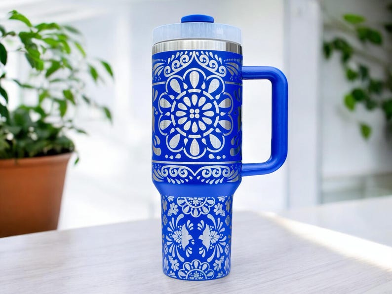 May include: A blue stainless steel travel mug with a white floral design. The mug has a handle and a lid.