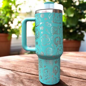 May include: A turquoise stainless steel travel mug with a handle. The mug is covered in a silver pattern of guinea pigs, hay, and other guinea pig-related items.