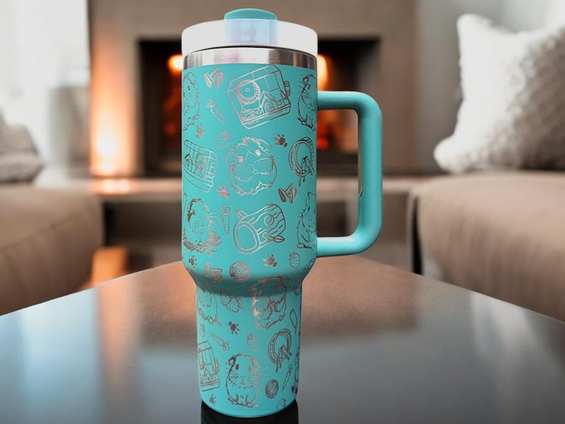 May include: A turquoise stainless steel travel mug with a silver lid and handle. The mug is decorated with a silver pattern of animals and trees.