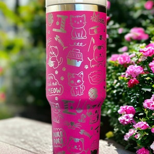 May include: A pink stainless steel tumbler with a silver cat-themed design. The tumbler features a variety of cat-related images, including cats, cat toys, and cat food bowls. The text "You had me at meow" is also included on the tumbler.