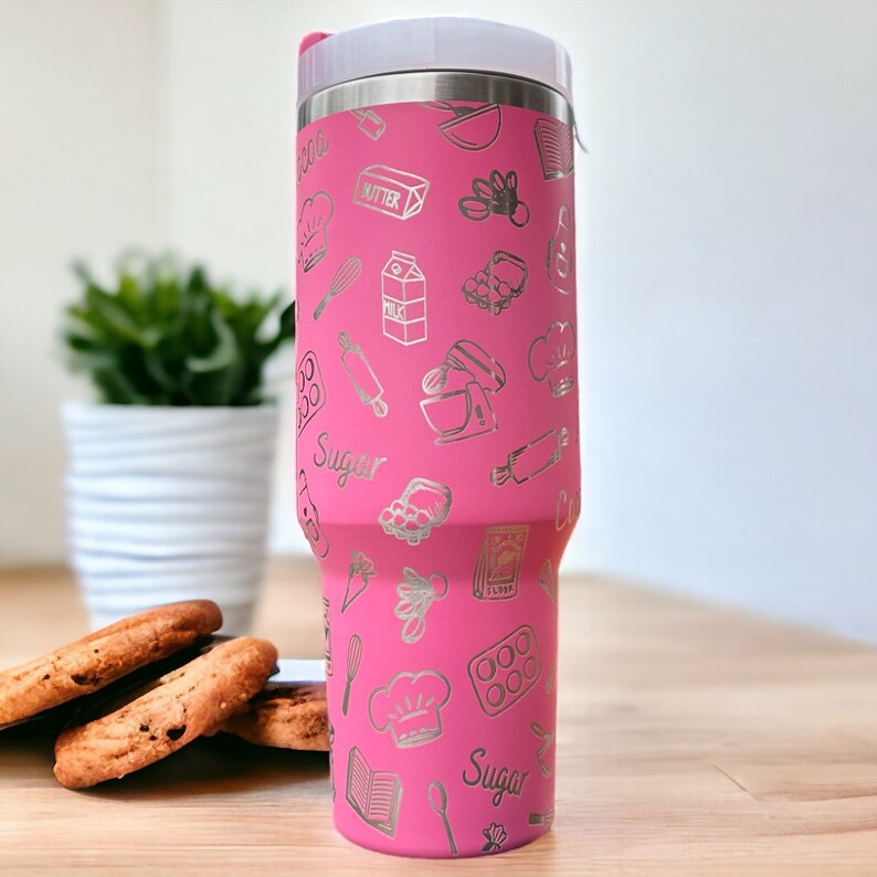 May include: Pink stainless steel tumbler with a silver design of baking-themed icons, including a whisk, rolling pin, and a chef's hat. The tumbler has the words "Sugar" and "Milk" printed on it.