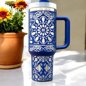 May include: A blue stainless steel travel mug with a silver patterned design. The mug has a lid and a handle.