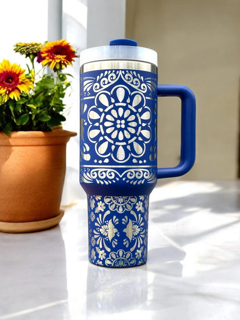 May include: A blue stainless steel travel mug with a silver patterned design. The mug has a lid and a handle.