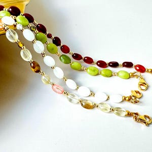 May include: Three strands of gemstone bead necklaces with gold accents. The necklaces feature red, green, and white oval-shaped beads.