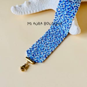 May include: A blue and white beaded bracelet with gold accents and a gold clasp. The bracelet is made with small, seed beads and has a geometric pattern.