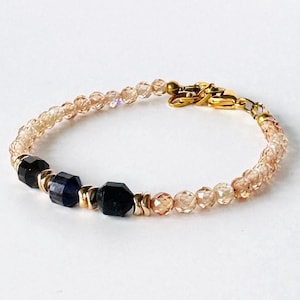 May include: A delicate bracelet with a gold clasp and a row of dark blue and black beads interspersed with small, clear, faceted beads.