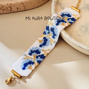 Peut inclure: Bracelet en perles blanches avec un motif géométrique bleu et or. Le bracelet a un fermoir en or.